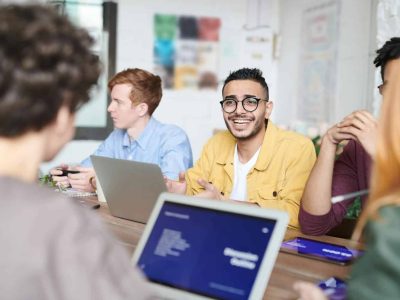 A diverse group discussing a project with laptops in a modern office meeting room.
